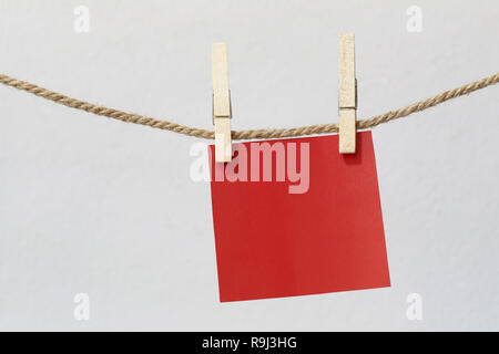 Red note paper hanging on rope on white wall and have clipping paths. Stock Photo