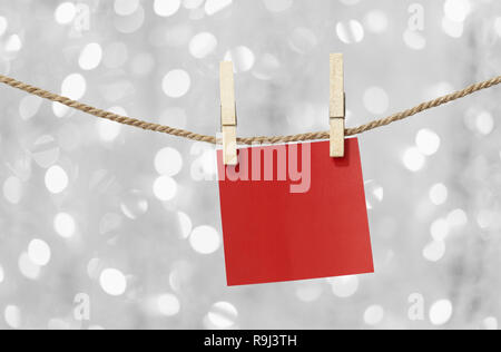 Blank red paper notes hanging on clothesline for design in Christmas Day on bokeh light background,Notepad for design ideas for Important day. Stock Photo