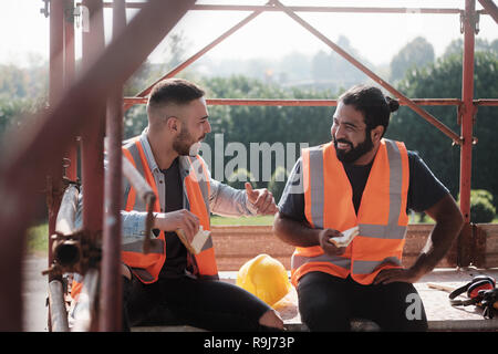 People working in construction site. Men at work in new housing project. Team of happy workers laughing, talking and eating snack during lunch break Stock Photo