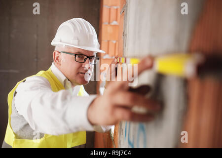 People working in construction site. Man at work in new home inside apartment building. Foreman using measuring tool on brick wall and typing data on  Stock Photo