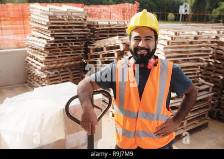 Skilled people working in construction site. Hispanic man at work in new house. Portrait of happy latino worker using manual forklift to move hardware Stock Photo