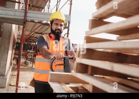 Skilled people working in construction site. Hispanic man at work in new housing project. Professional latino worker using manual pallet jack to move  Stock Photo