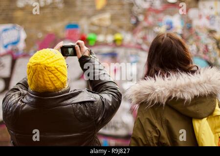 Two women taking a photo of a wall of graffiti in Brick Lane, East London Stock Photo