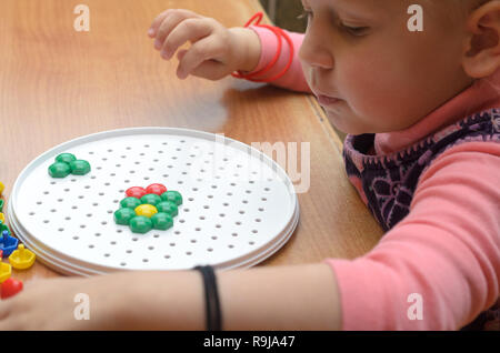 A little girl collects a colorful mosaic at the table Stock Photo
