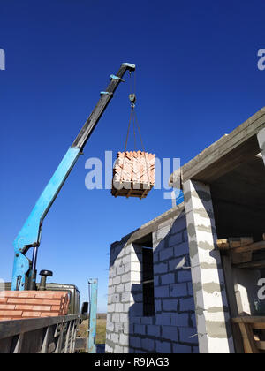 The crane raises a brick on the back of a blue sky 2018 Stock Photo