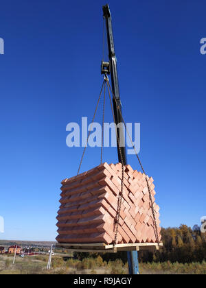 The car crane holds and unloads the brick on the background of the blue autumn sky 2018 Stock Photo