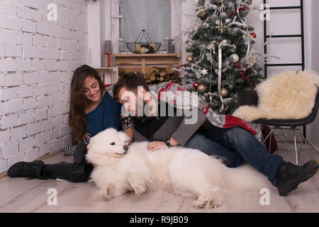 young beautiful couple having fun with their dog on the background of the New Year and Christmas decor. Family with Samoyed celebrate Stock Photo