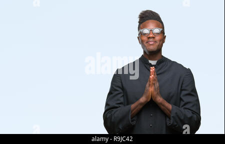 Young african american priest man over isolated background praying with hands together asking for forgiveness smiling confident. Stock Photo