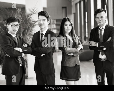 portrait of a group of young asian business people standing in office arms crossed, looking at camera smiling, black and white. Stock Photo