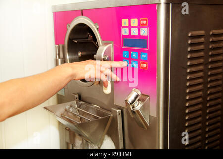 Female confectioner in chef uniform producing ice cream with ice cream machine at ice cream factory. Woman is push start button and programming. Stock Photo
