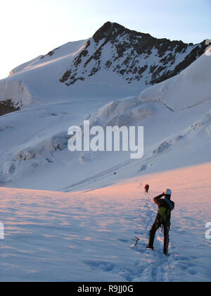 mountain climber on a rope standing on a large glacier stops to take a photo of the beautiful landscape just after sunrise Stock Photo