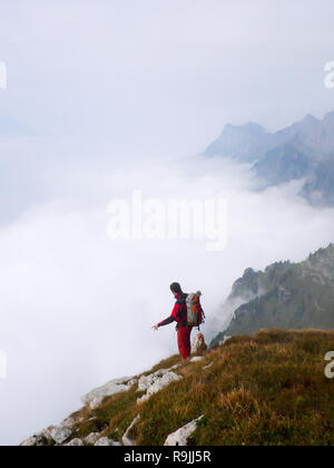 man stands at the end of a mountain cliff and looks down into a vast sea of cloud cover in the valley Stock Photo