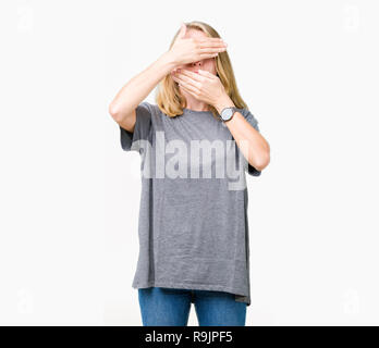 Beautiful young woman wearing oversize casual t-shirt over isolated background Covering eyes and mouth with hands, surprised and shocked. Hiding emoti Stock Photo