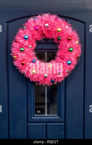 Fluorescent Pink Christmas wreath with baubles decoration on a blue cottage front door in Deddington, Oxfordshire, England Stock Photo