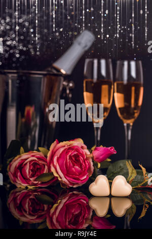 Champagne bottle in bucket with two wine glasses,  bouquet of roses and heart shaped chocolates with lights on black background. Love, Valentines day  Stock Photo