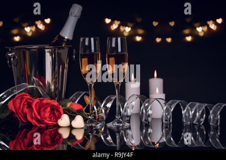 Champagne bottle in bucket with two wine glasses,  bouquet of  roses,  heart shaped chocolates and candles with lights on black background. Love, Vale Stock Photo
