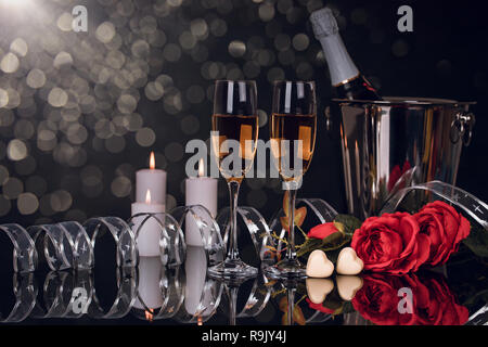 Champagne bottle in bucket with two wine glasses,  bouquet of  roses,  heart shaped chocolates and candles wiht lights on black background. Love, Vale Stock Photo