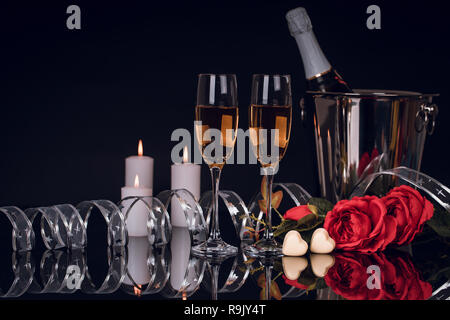 Champagne bottle in bucket with two wine glasses,  bouquet of  roses,  heart shaped chocolates and candles on black background. Love, Valentines day c Stock Photo