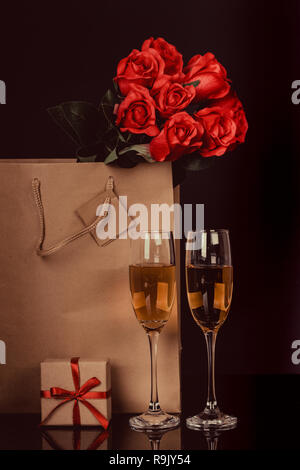 Champagne bottle in a paper bag, two wine glasses and  red roses on black background. Love, Valentines day concept Stock Photo
