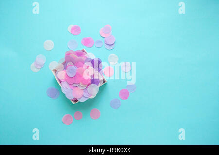 Flat lay of box full of colorful confetti on pastel blue and pink background with copyspace. Stock Photo