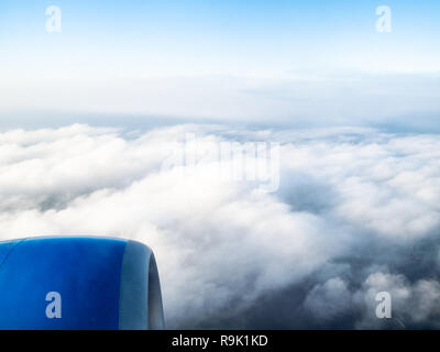 view of airplane engine over dense gray clouds in blue sky during flight through porthole Stock Photo