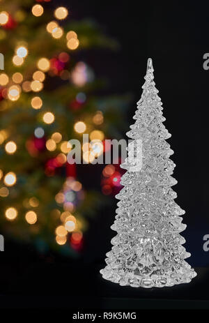 Crystal glass christmas tree in front of a real christmas decorated with multicolored lights Stock Photo