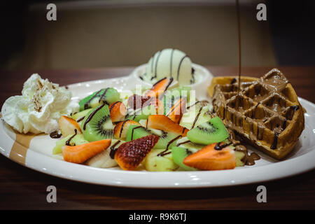 Classic Belgian waffle, served with slices of strawberry, banana, kiwi and pineapple.  Drizzled with rich chocolate, served with ice-cream on the side Stock Photo