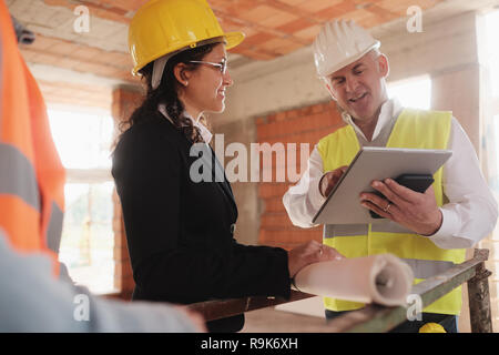 Men and woman working in construction site. Teamwork with worker speaking with foreman and engineer and looking at blueprints during business meeting Stock Photo