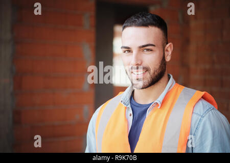Skilled people working in construction site. Young man at work in new house. Portrait of happy white manual worker with protective workwear smiling at Stock Photo