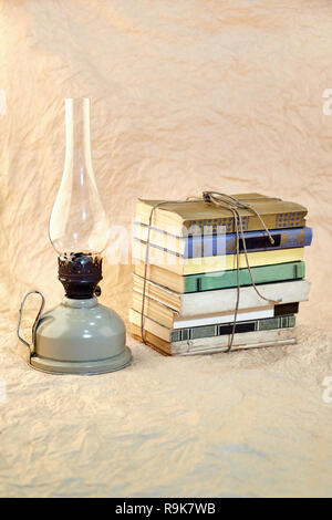 Kerosene lamp and stack of old books tied up with string. Stock Photo