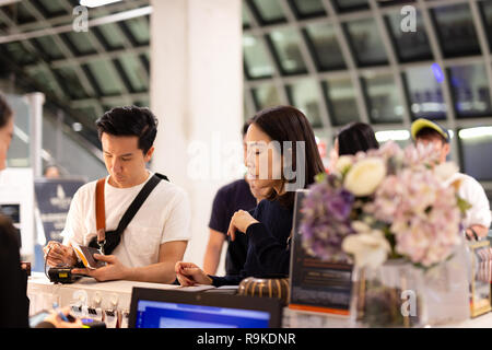 Asian couple signing bill for hotel room at reception. Stock Photo
