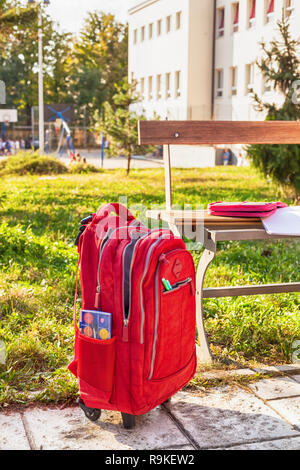 Modern red weightless school bag by the bench on the schoolyard Stock Photo