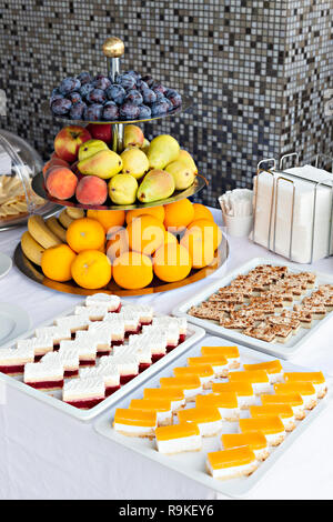 Small chocolate and vanilla layered cakes lined up iin rows on candy buffet with fruit. Sweet paradise. Stock Photo