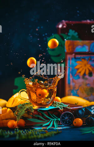 Citrus tea with a dynamic splash. Mango, oranges, kumquat, and other tropical fruits in a dark still life with copy space. Stock Photo