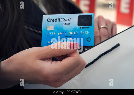Close up of female hands holding face of credit card and shopping bag at mall background. Readable details of credit card information in lady's hands. Stock Photo