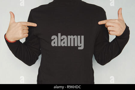 Cropped shot of good-looking young unshaven man wearing casual clothes, pointing fingers at copy space on his black blank t-shirt. Clothing, design, s Stock Photo