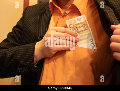 businessman in suit and vivid orange shirt putting fifty 50 euros in his shirt pocket. closeup image Stock Photo