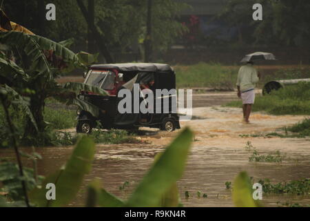 A Rickshaw travels along a submerged road during heavy rain and flood in Kerala in 2018 as a person holding umbrella walks by. Stock Photo