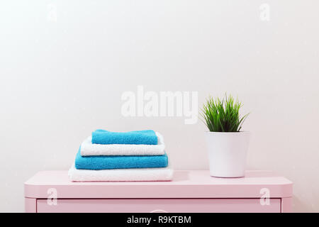 On a pink dresser there is a pile of towels and a home plant stands Stock Photo