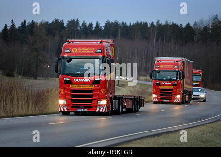 Salo, Finland - December 14, 2018: Fleet of red Next Generation Scania S500 semi trailer trucks of Translog on the road in Finland on cloudy evening. Stock Photo
