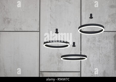 Unusual light sources hang on the background of a marble wall. Lamps in the form of a luminous ring Stock Photo