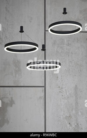 Unusual light sources hang on the background of a marble wall. Lamps in the form of a luminous ring Stock Photo