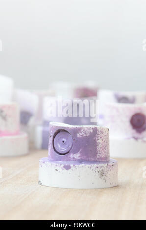 Several plastic nozzles from a paint sprayer that lie on a wooden surface against a gray wall background. The caps are smeared in violet paint. The co Stock Photo