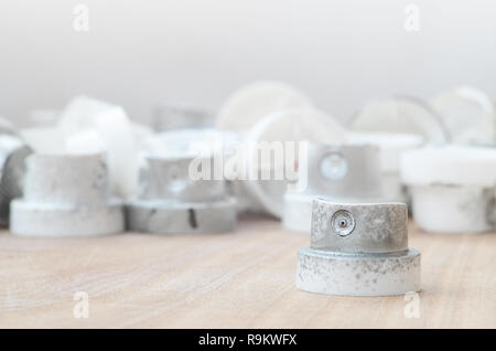 Several plastic nozzles from a paint sprayer that lie on a wooden surface against a gray wall background. The caps are smeared in chrome paint. The co Stock Photo