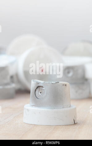 Several plastic nozzles from a paint sprayer that lie on a wooden surface against a gray wall background. The caps are smeared in chrome paint. The co Stock Photo
