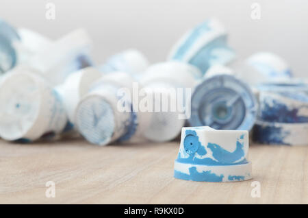 Several plastic nozzles from a paint sprayer that lie on a wooden surface against a gray wall background. The caps are smeared in blue paint. The conc Stock Photo