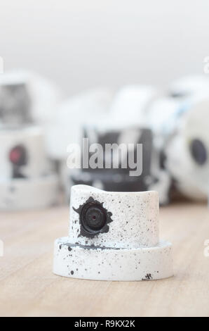 Several plastic nozzles from a paint sprayer that lie on a wooden surface against a gray wall background. The caps are smeared in black paint. The con Stock Photo