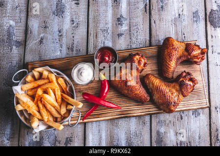Grilled chicken wings, french fries, white and red sauce nuts on a wooden surface Stock Photo
