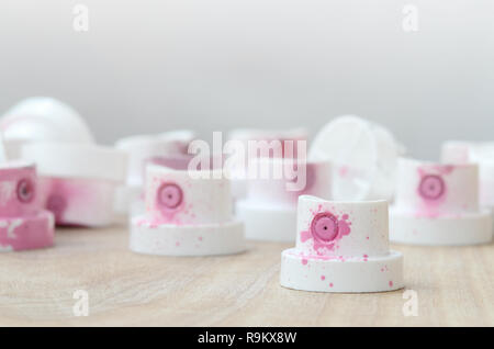 Several plastic nozzles from a paint sprayer that lie on a wooden surface against a gray wall background. The caps are smeared in pink paint. The conc Stock Photo