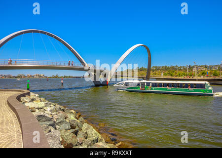 Perth, Australia - Jan 3, 2018: Turistic ferry crossing iconic Elizabeth Quay Bridge on Swan River. Scenic landscape seen from wooden walkway of arched pedestrian bridge of Elizabeth Quay marina. Stock Photo